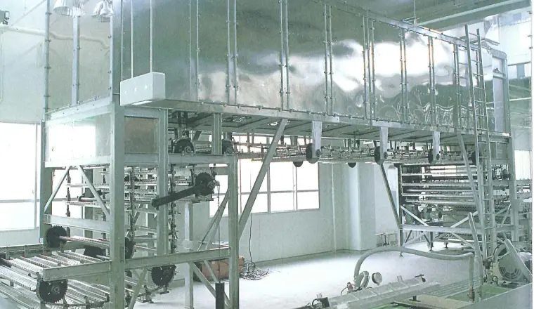 工場内に設置された大型の産業用設備（製造ライン）の写真。金属製の機械と搬送装置が並んでいる。