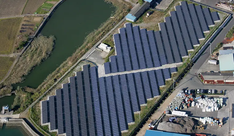 水路の脇に大規模な太陽光パネルが並ぶ太陽光発電所を上空から撮影した写真。