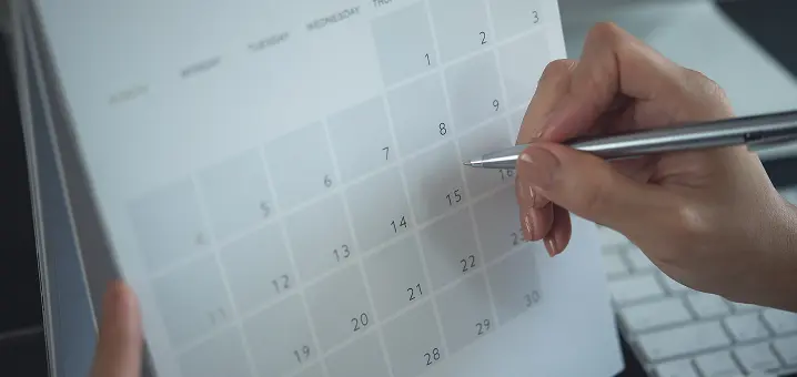 タブレットに表示されたカレンダー画面に、ペン先を当てて予定を書き込もうとしている手元。