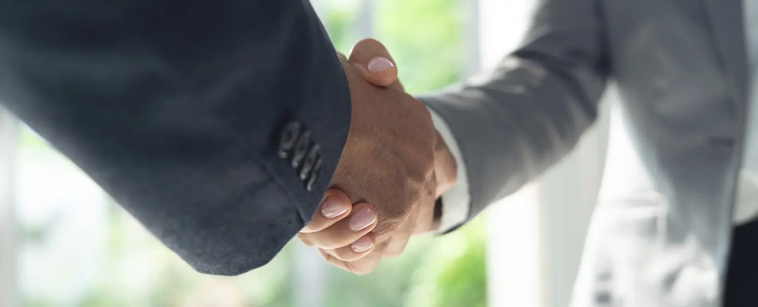スーツ姿の2人が握手をしている手元のクローズアップ。背景はぼかした明るい室内。