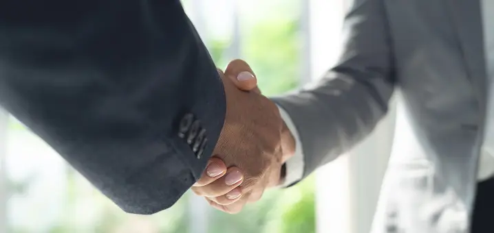 スーツ姿の2人が握手をしている手元のクローズアップ。背景はぼかした明るい室内。