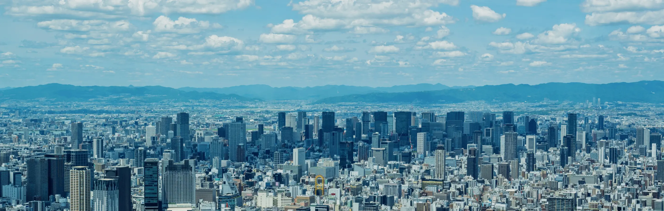 大阪の都市風景。高層ビルが立ち並び、遠くに山並みが見える晴天のパノラマ