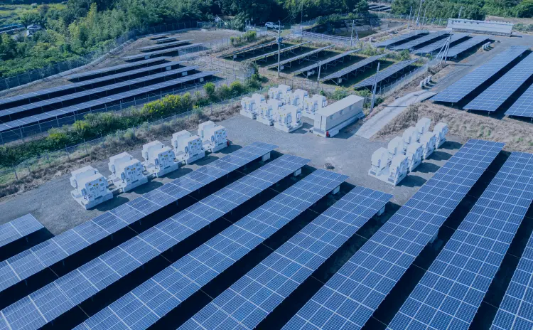 整列したパネルのあいだに白いコンテナ型の蓄電・電力設備が配置されている空からの風景